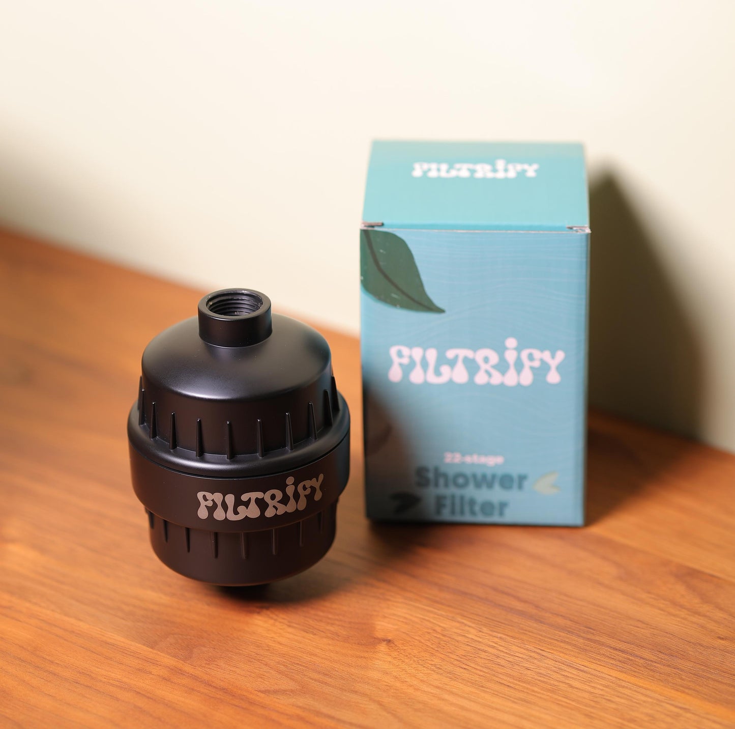 A Filtrify shower filter next to its packaging box on a wooden surface.